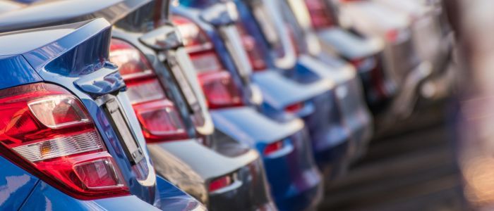 A row of blue cars are parked next to each other in a parking lot.