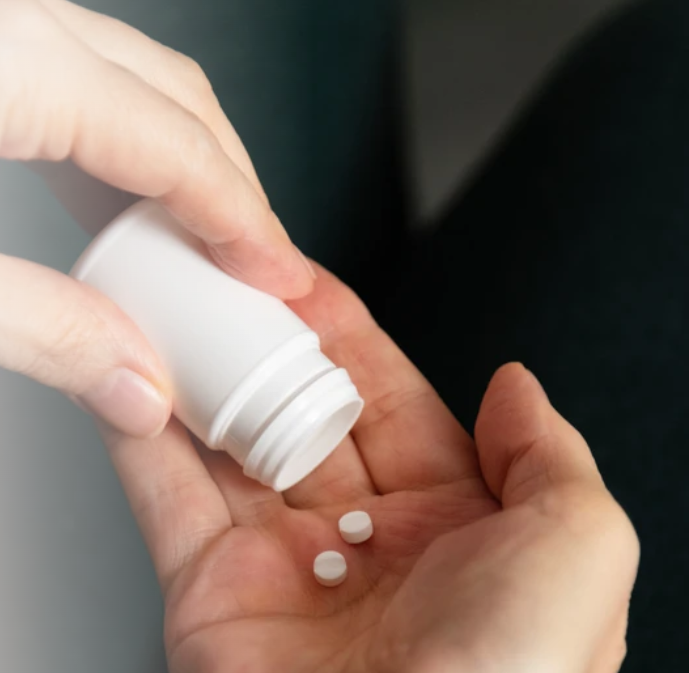 Hand pouring two white pills from a bottle into an open palm