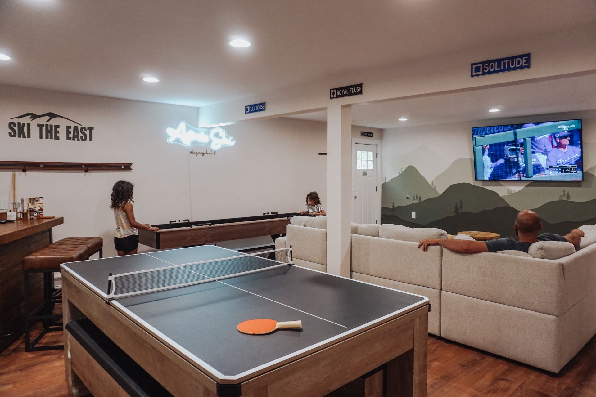 Game room with ping-pong table, pool table, couch, and wall-mounted TV in a modern lounge