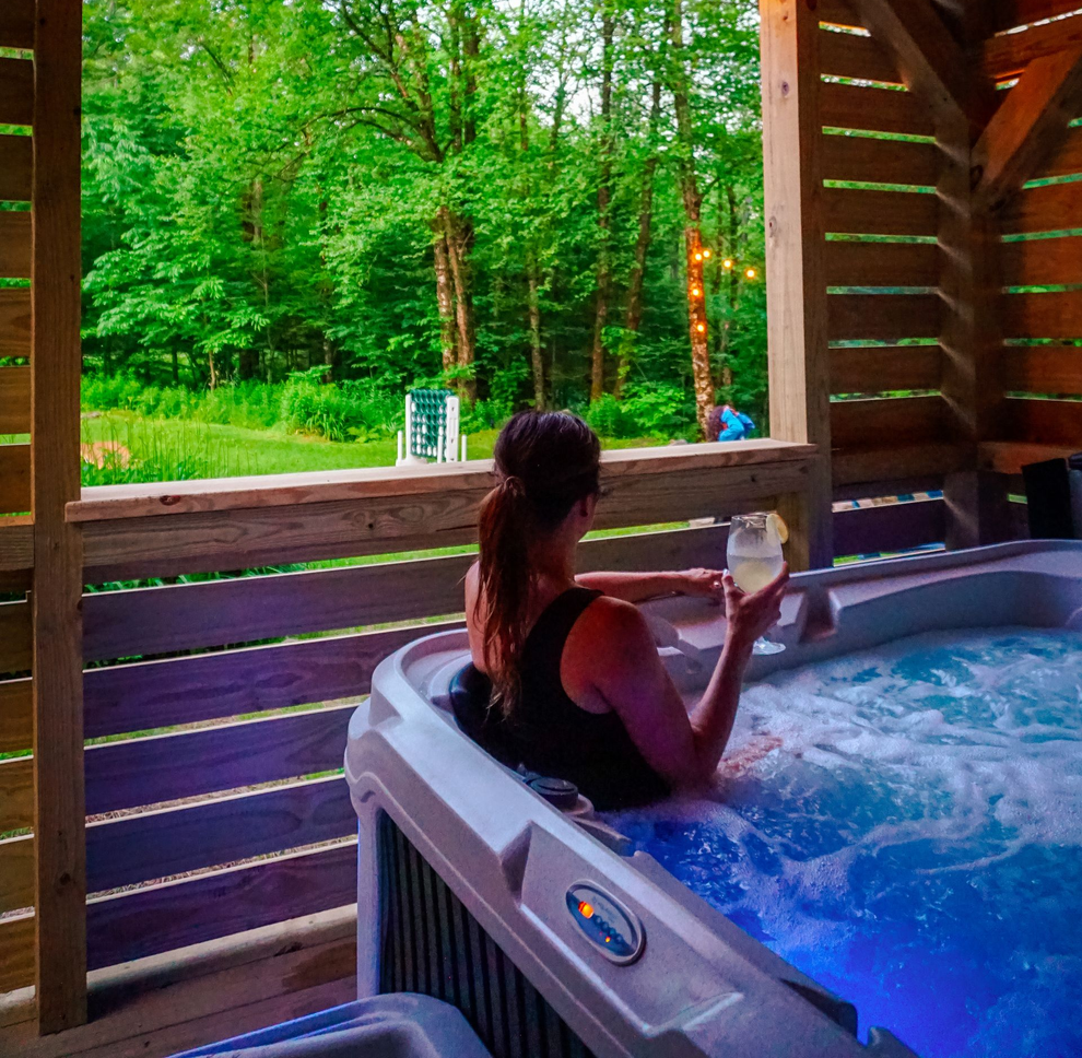 Woman relaxing in a hot tub on a wooden porch overlooking a green forest