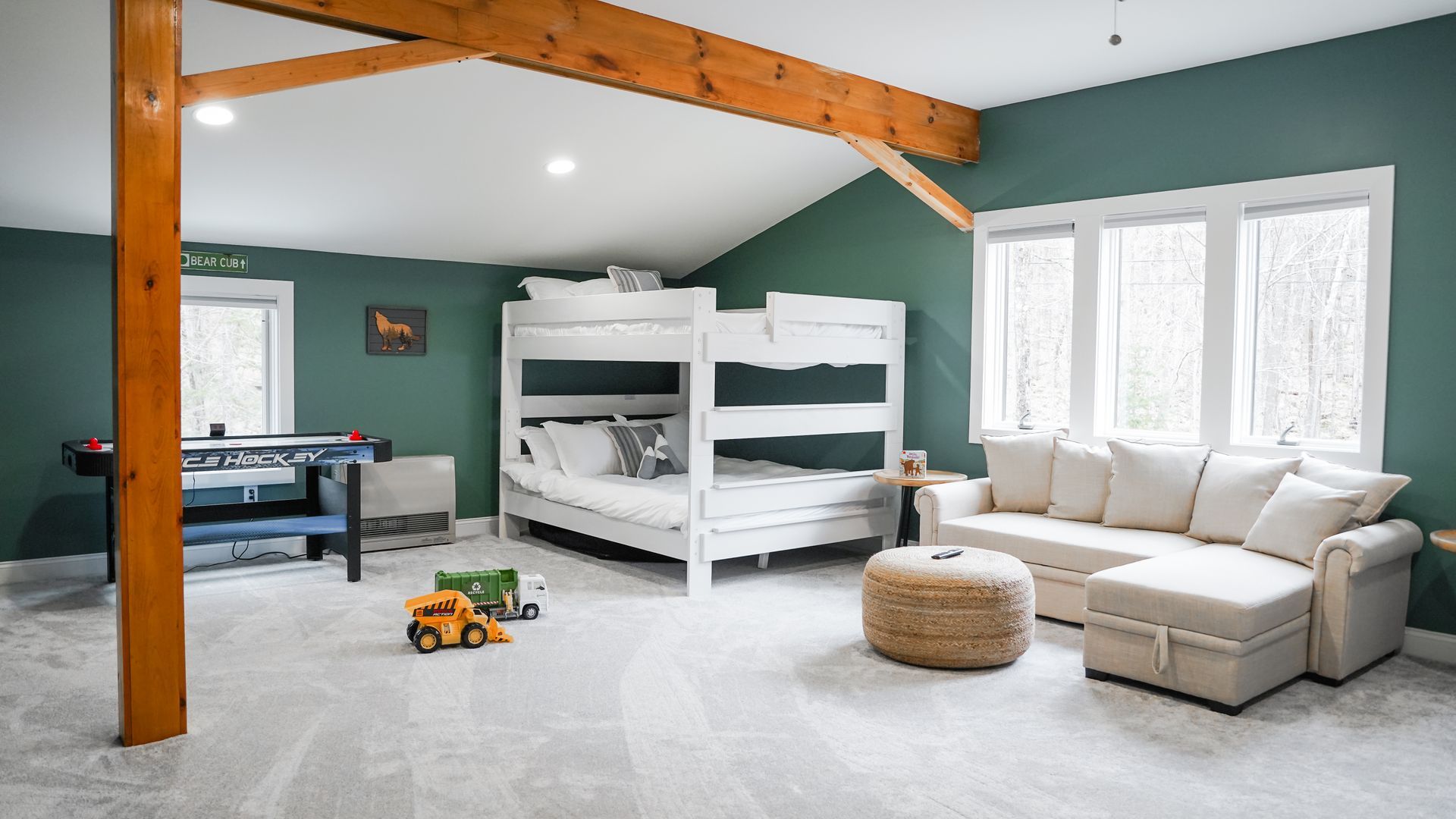 Bright playroom with bunk beds, sofa, toy truck, and white windows under a sloped wood-beam ceiling