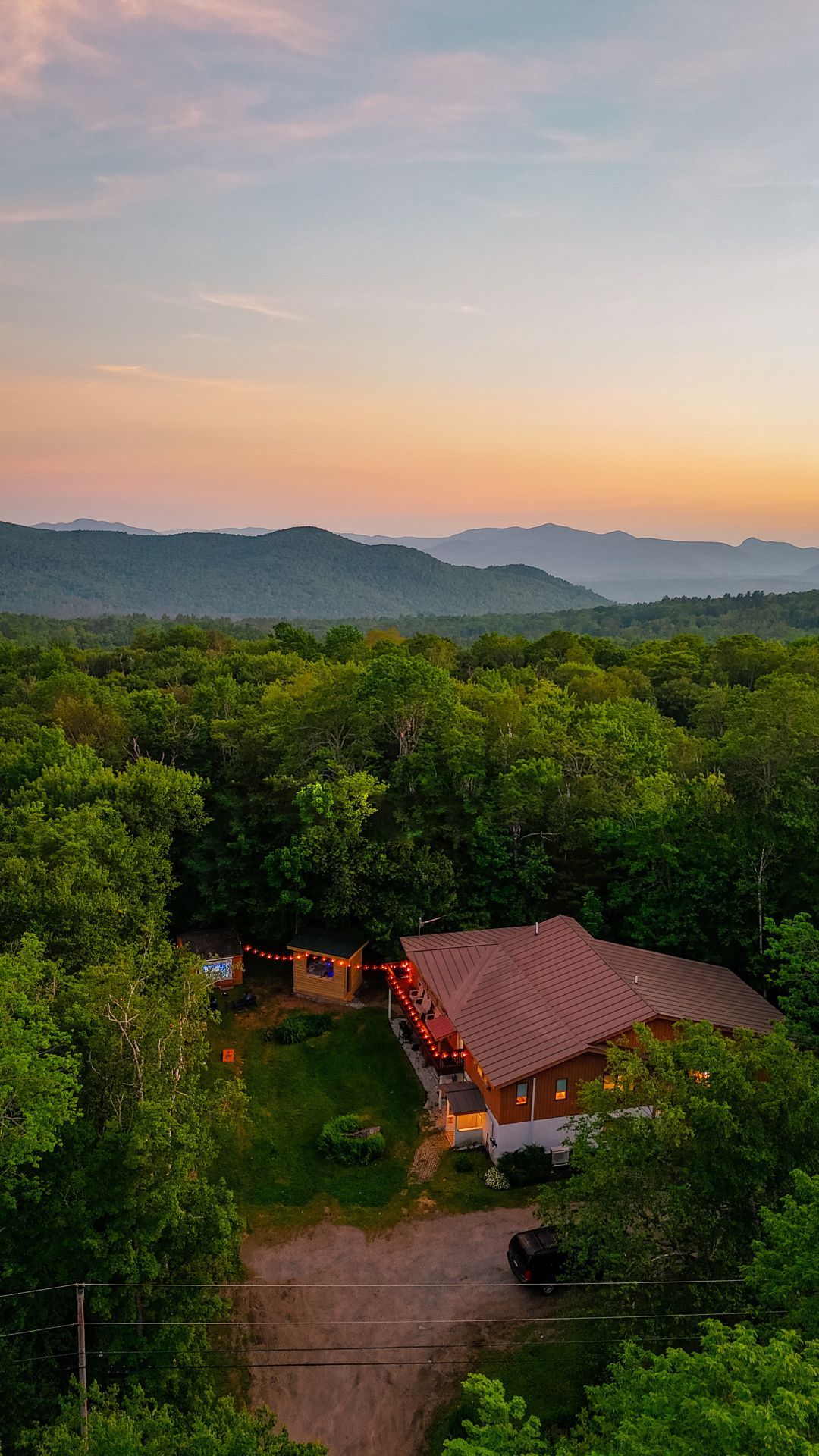 Sunset over a lush Vermont forest with a cabin and lit patio below.