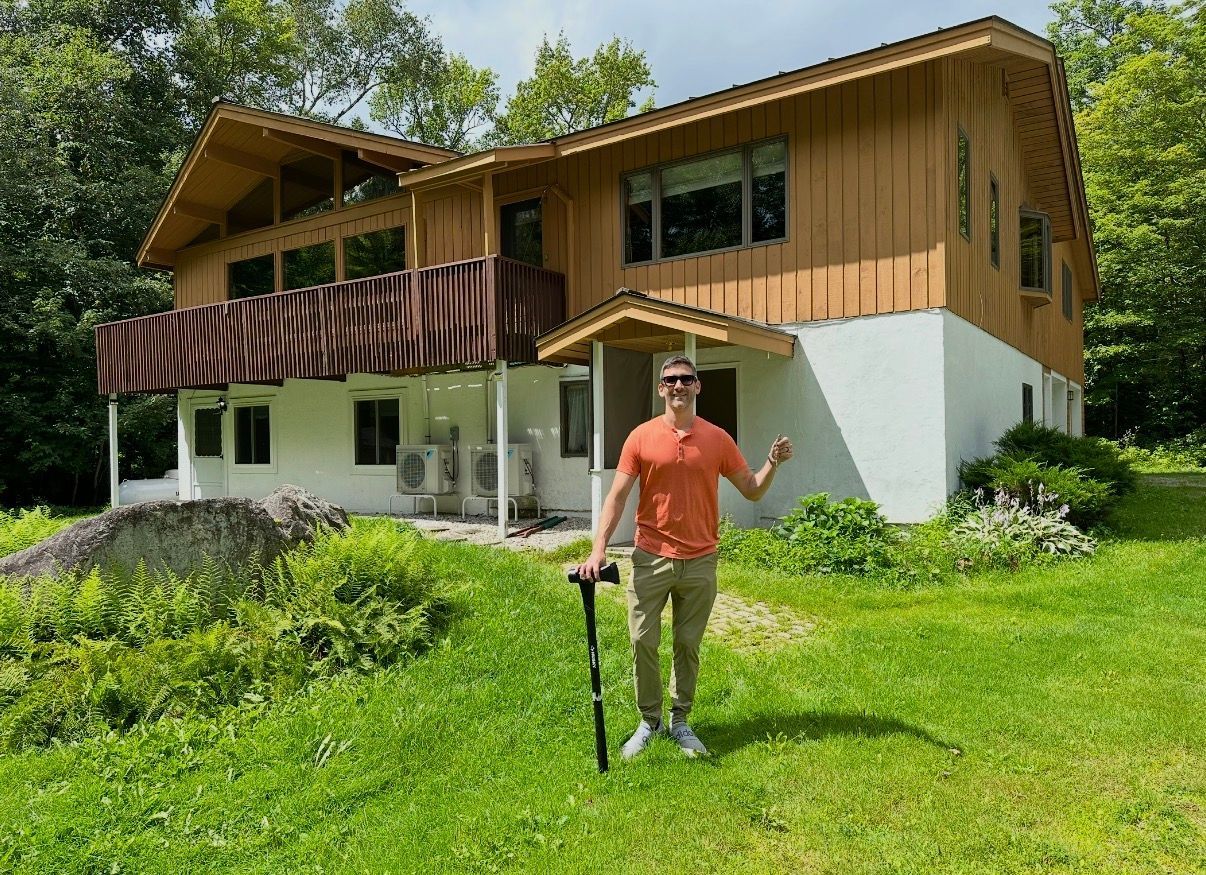 Person in orange shirt standing on lawn in front of a wooden house with a striped awning.