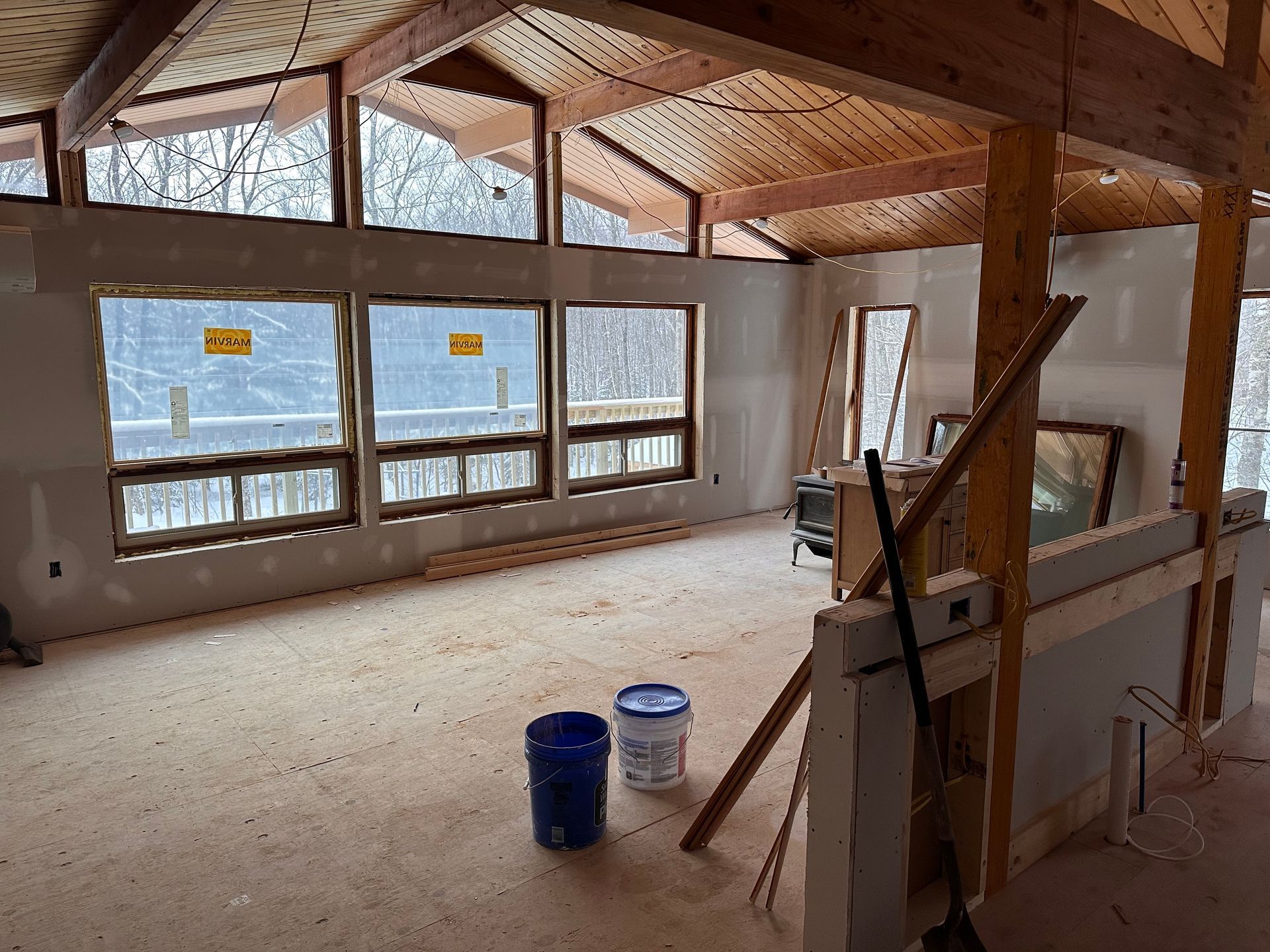 Unfinished room with exposed wooden beams, large windows, and paint buckets on the floor