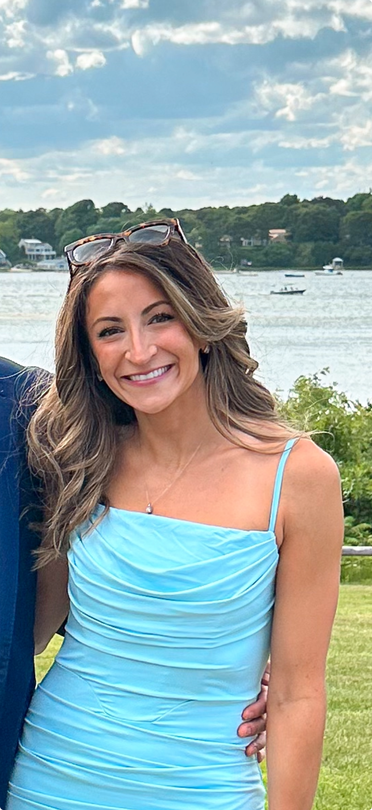 Smiling woman in a light blue dress by the water under a cloudy sky