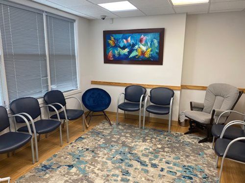 Waiting room with blue chairs, a patterned rug, and a colorful fish painting on the wall.