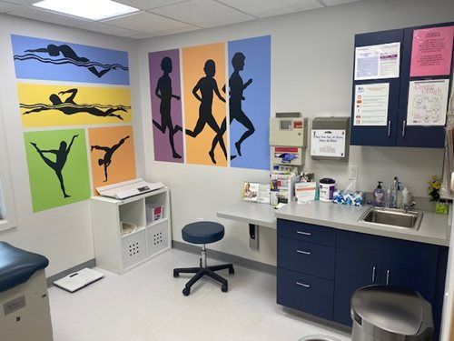 Clinic room with colorful dancer posters, exam chair, sink, cabinets, and bulletin board on the wall