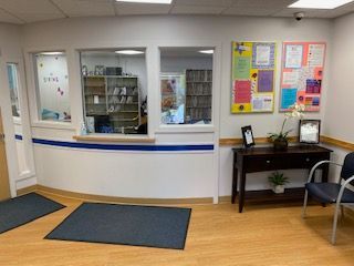 Office reception area with service window, blue-striped counter, bulletin boards, and seating.