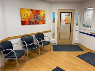 Waiting room with three chairs, colorful wall art, and a door with a window.