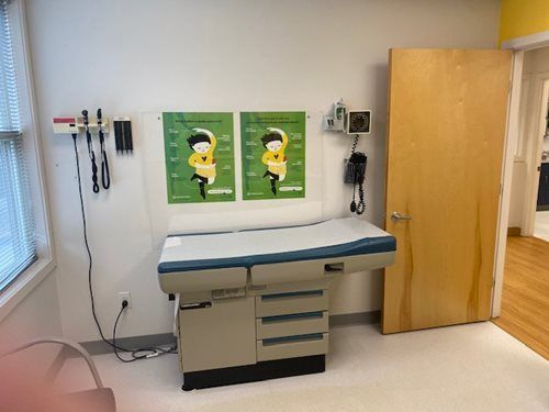 Exam room with exam table, medical tools on wall, posters, and open cabinet door