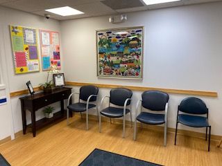 Waiting room with blue chairs, a side table, and colorful wall art on beige walls.