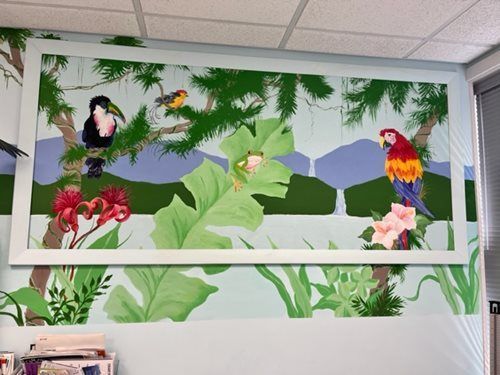 Tropical bird mural with parrots, toucan, and green leaves above a counter in a bright room