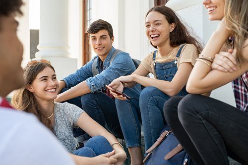 A group of friends sitting on steps outdoors, smiling and chatting together
