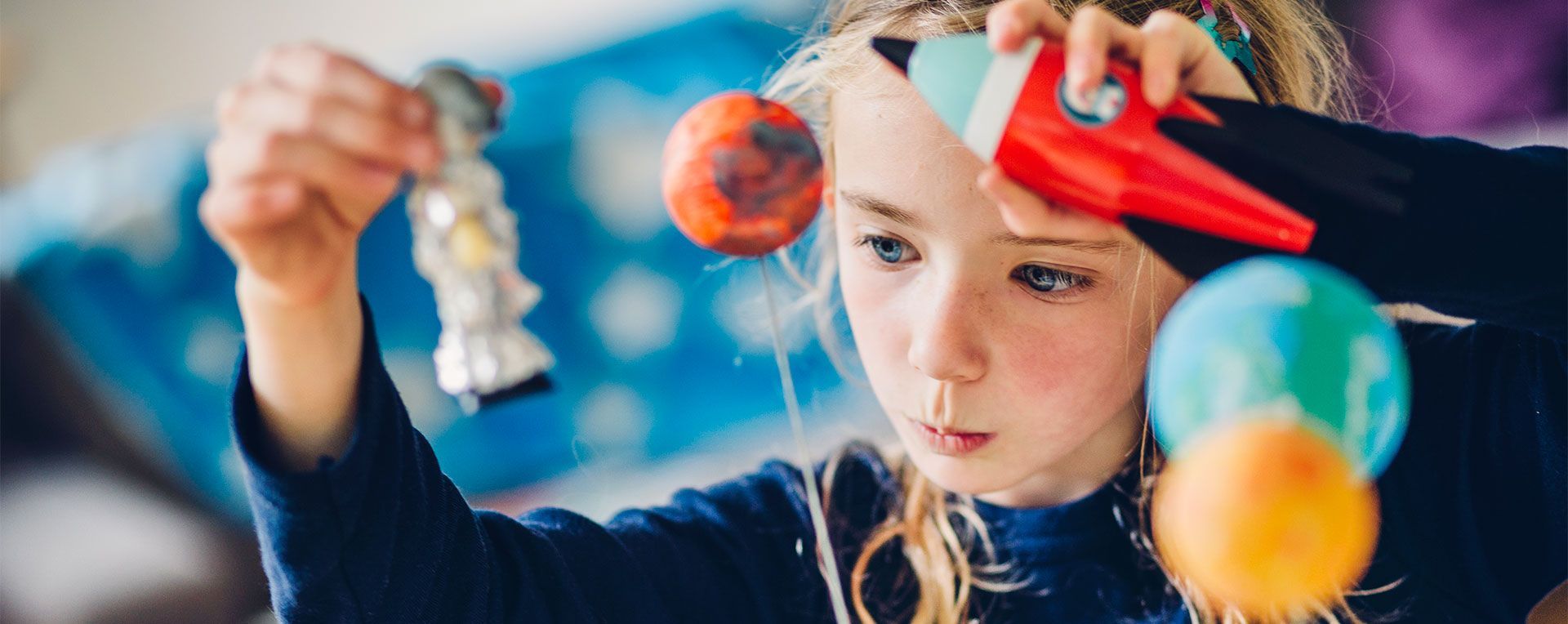 Child concentrating on a colorful solar system model with hanging planets