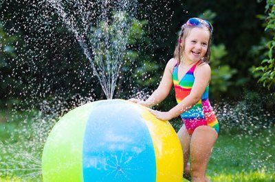 Child playing with a colorful inflatable ball and spraying water outdoors in a grassy yard