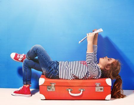 Child lying on a red suitcase, playing a recorder against a blue background.