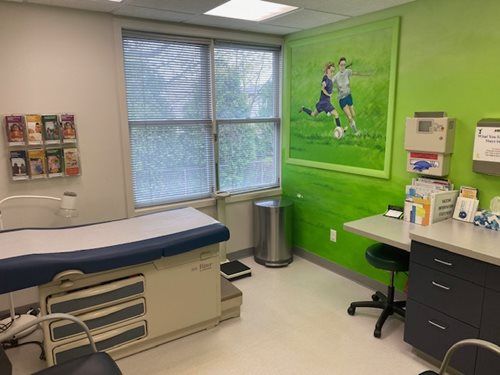 Medical exam room with exam table, window, sink, and bright green wall art