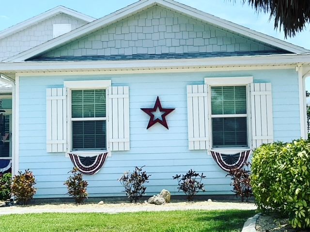 Light blue house with white shutters, patriotic bunting under two windows, and a large red star mounted on the siding.