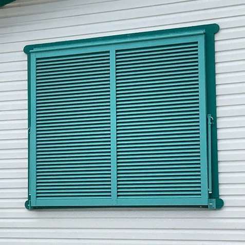 A set of teal-colored louvered window shutters mounted on white horizontal siding.