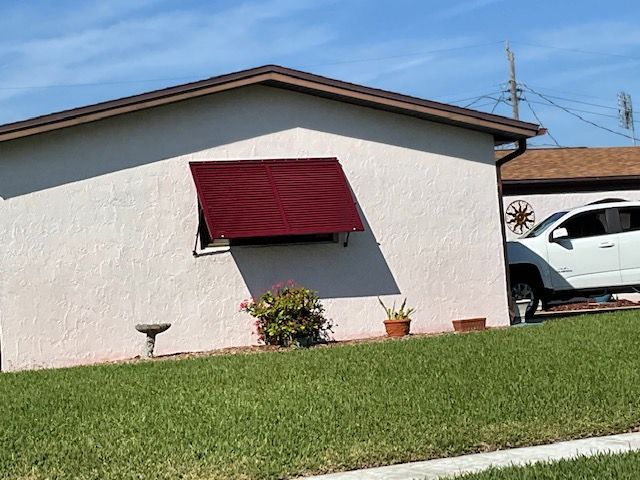 A low-slung beige house with a prominent maroon awning over a window, a small garden, and a white SUV parked nearby.