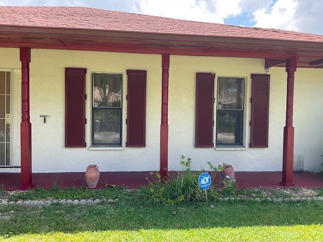 A house exterior with cream walls, a red roof, red porch posts, and two windows with red shutters.