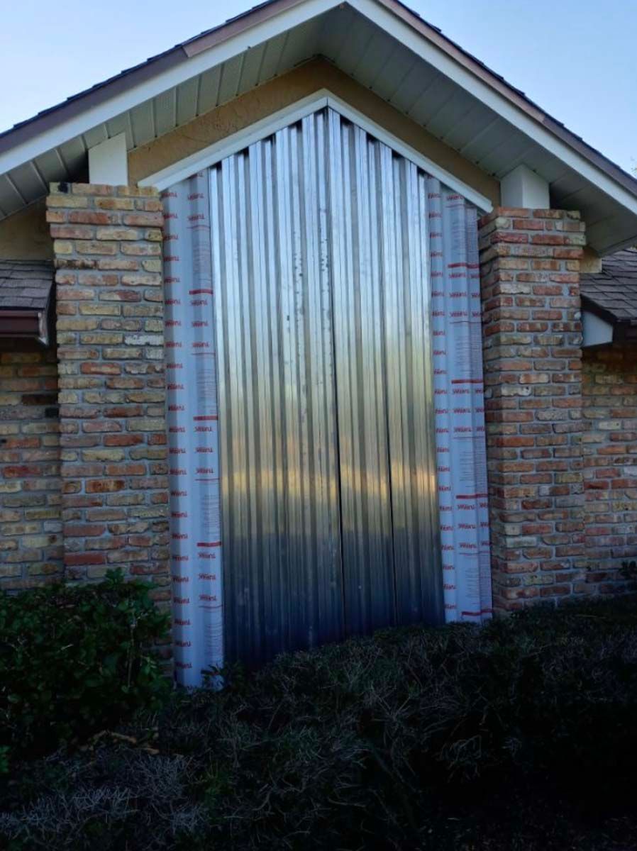 Corrugated metal panels are installed over a tall, arched brick entryway of a home.