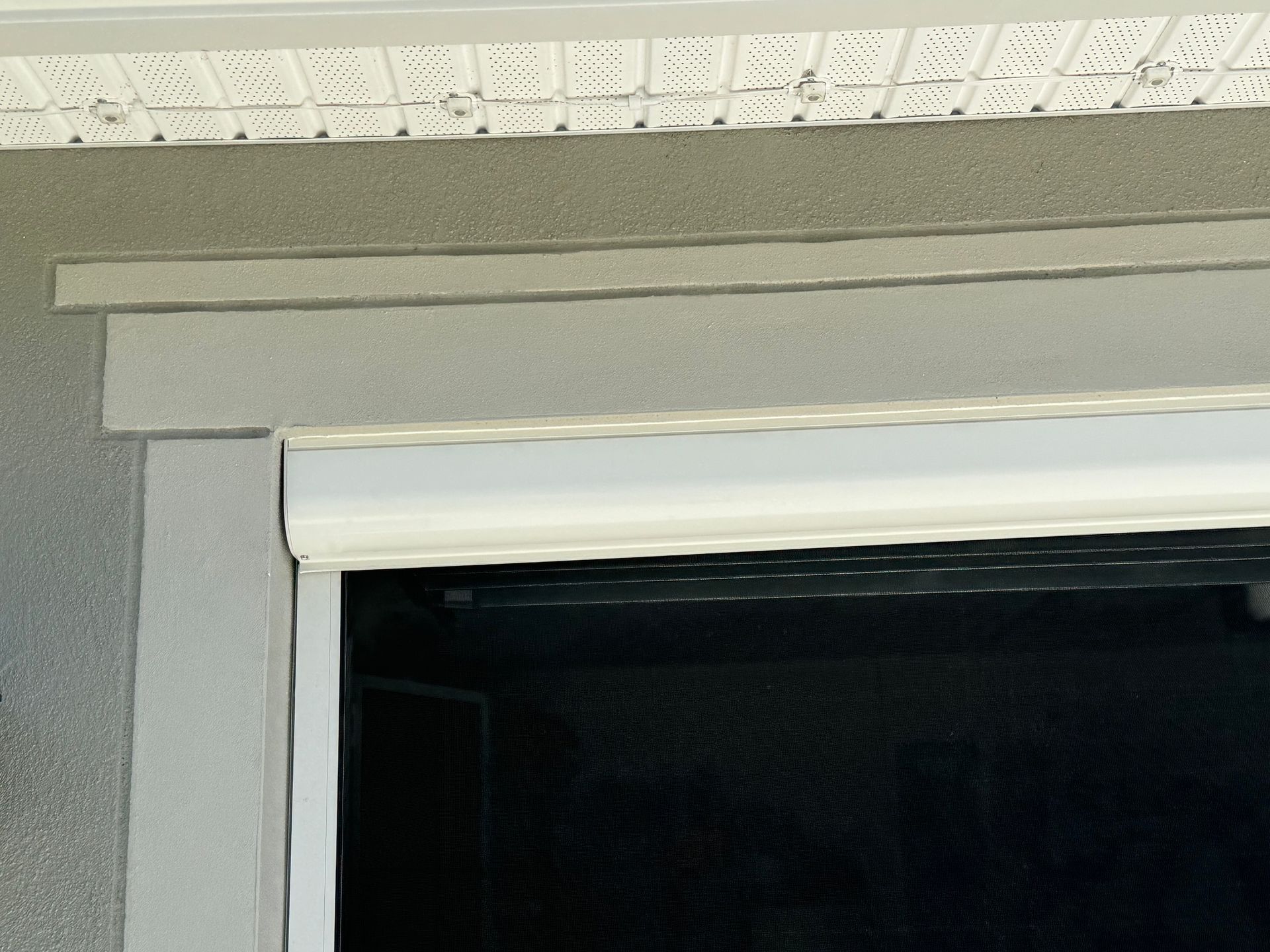 A close-up view of beige exterior trim around a garage door frame, positioned beneath a white vented soffit.