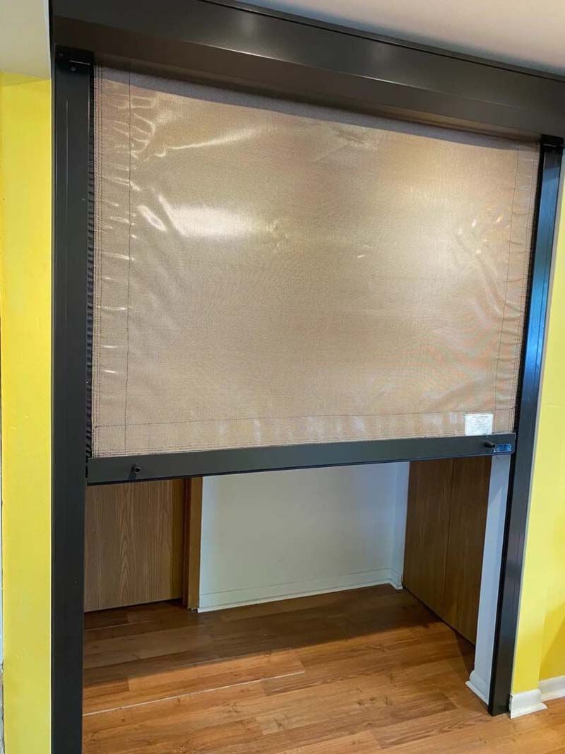 A pull-down plastic screen hangs in a dark frame between yellow walls, partially obscuring a doorway.