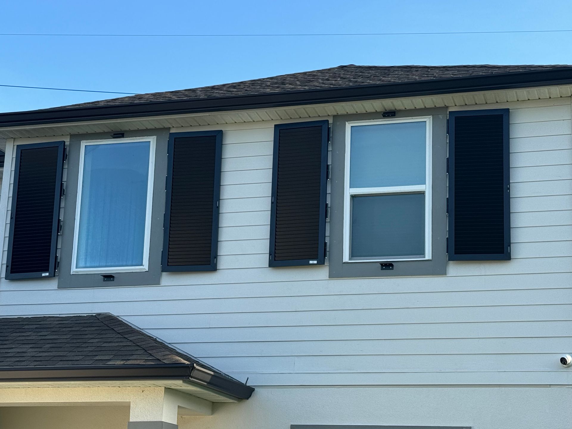 Two windows with dark shutters on the upper story of a house with light gray horizontal siding.