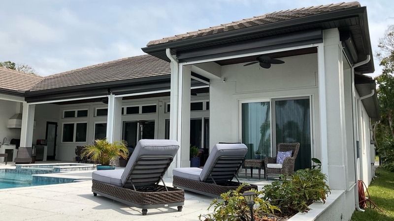 A backyard patio with two lounge chairs facing a swimming pool next to a white house with a covered lanai.