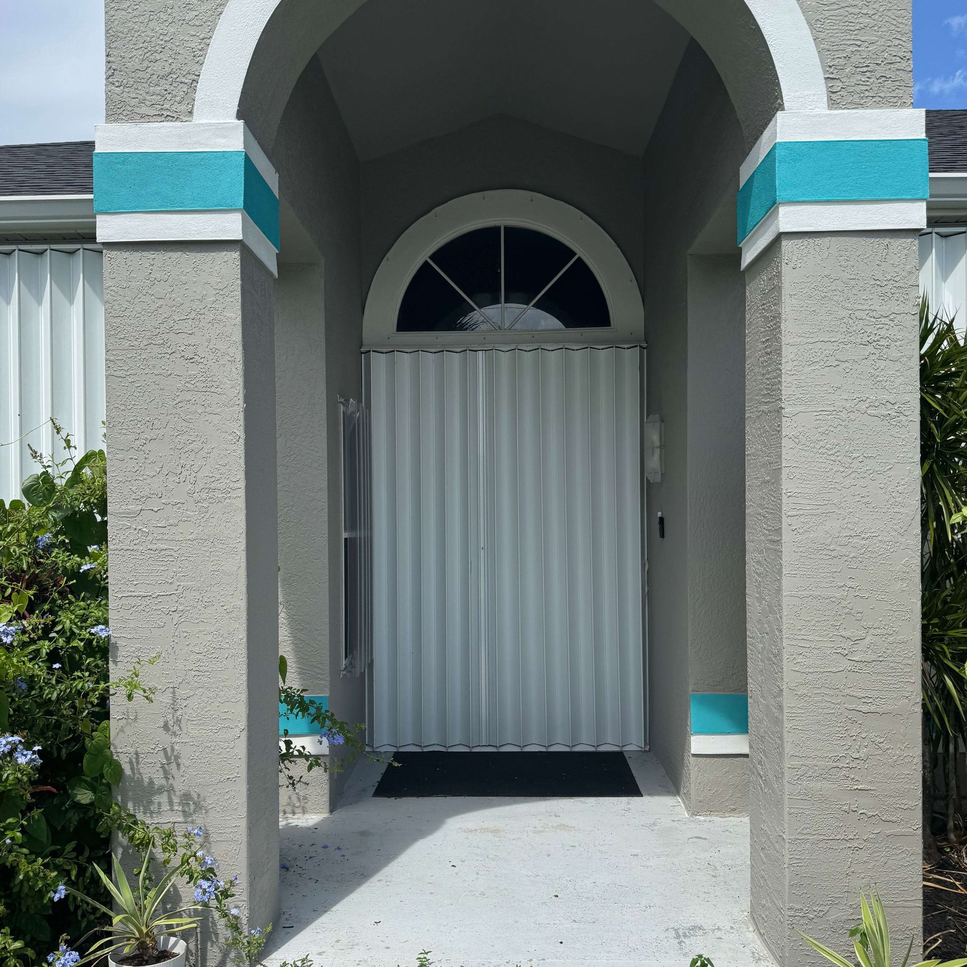 An entryway with textured gray pillars featuring horizontal turquoise stripes, leading to a closed white accordion door.
