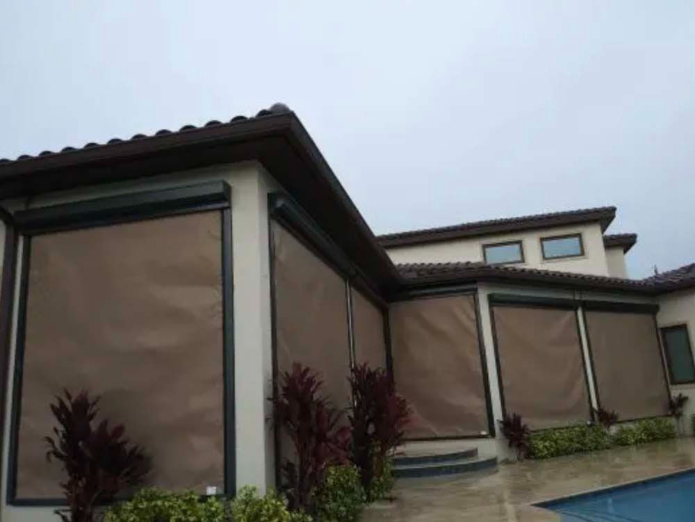 A patio with outdoor roller shades installed on a house exterior next to a swimming pool.