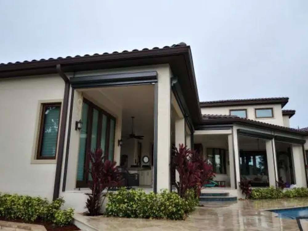 A cream-colored home with dark trim and a swimming pool, featuring an open, covered patio area with dark screen frames.