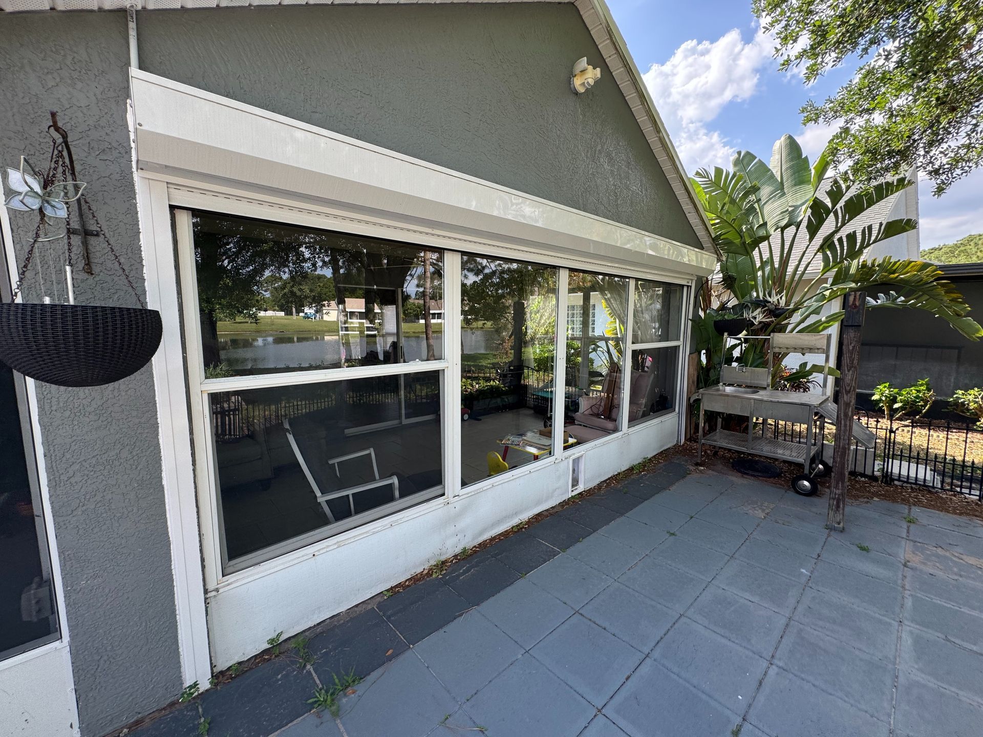A gray stucco house exterior with a large screened-in porch, glass sliding doors, and a tiled patio under a sunny sky.