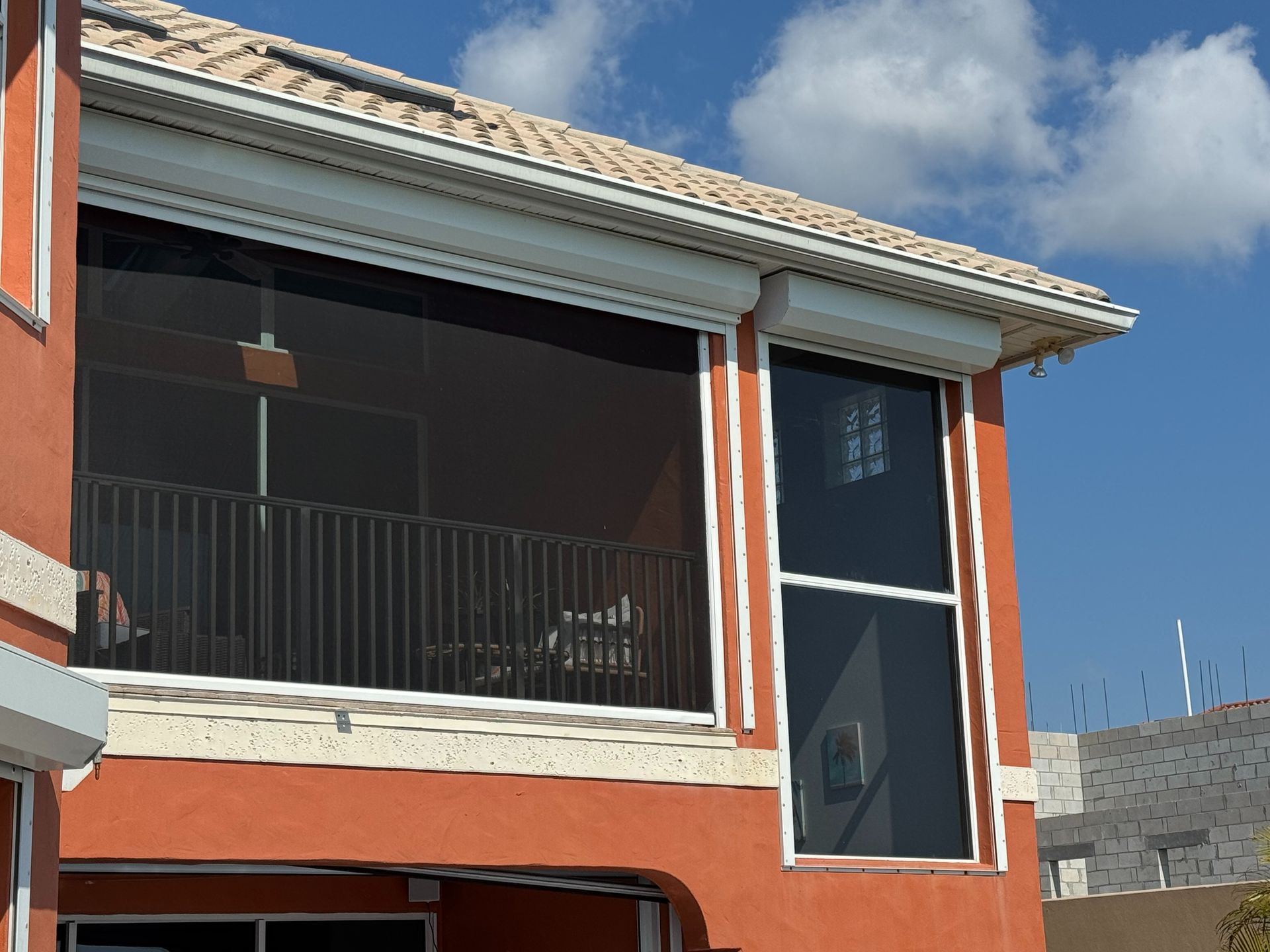A corner view of an orange house featuring a balcony and window fitted with retractable dark solar screens.