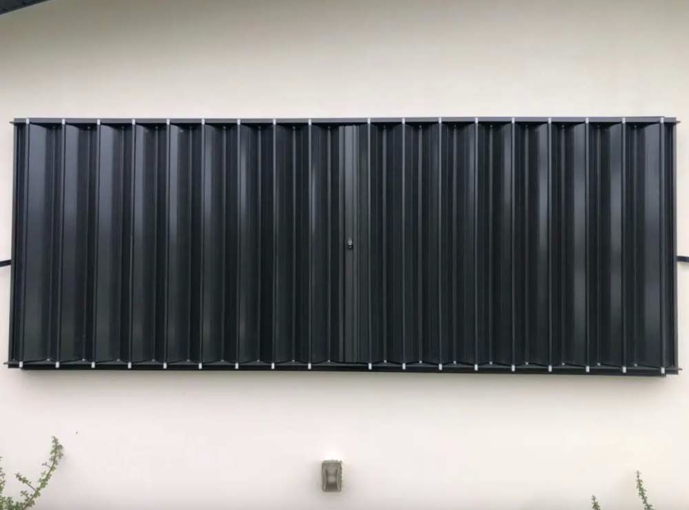 A rectangular, dark-colored solar thermal wall collector mounted horizontally on a beige exterior wall.