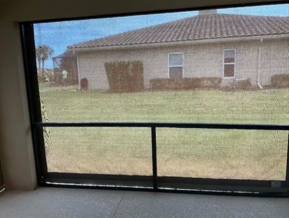 A view of a tan, single-story house with a tile roof seen through a black framed screen enclosure.