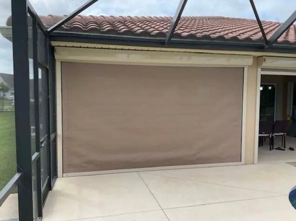 A tan, retractable privacy shade installed over a patio opening beneath a tiled roof.