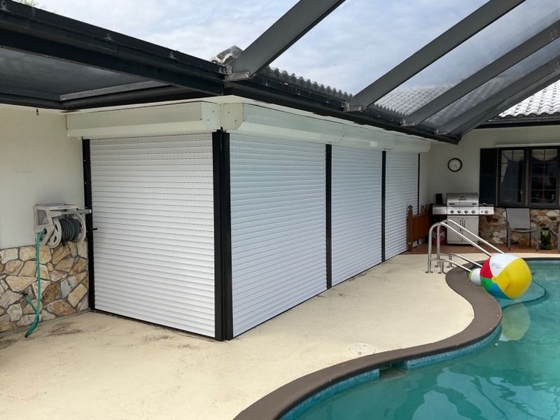 White rolling security shutters covering a wall by a curved backyard swimming pool.