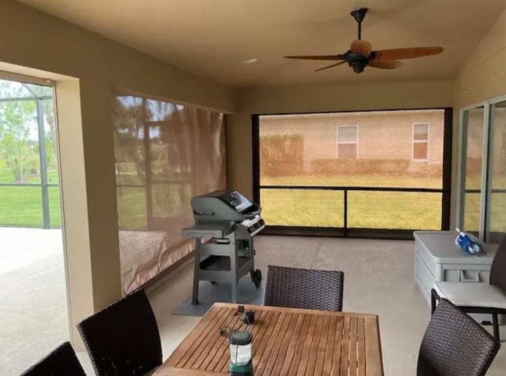 A screened-in patio with a dining table, a grill, a ceiling fan, and a view of a grassy yard.