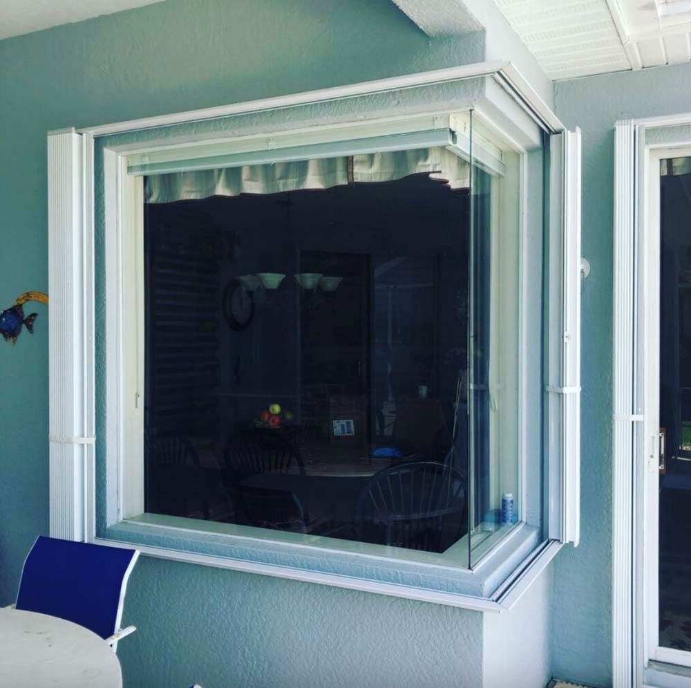 A white, rectangular bay window on a light blue wall, reflecting the interior of a room with a table and chairs.