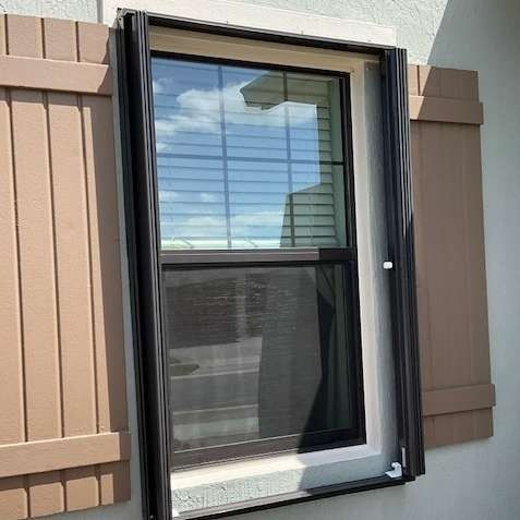 A black metal frame mounted around a window on a tan wall with brown shutters on either side.
