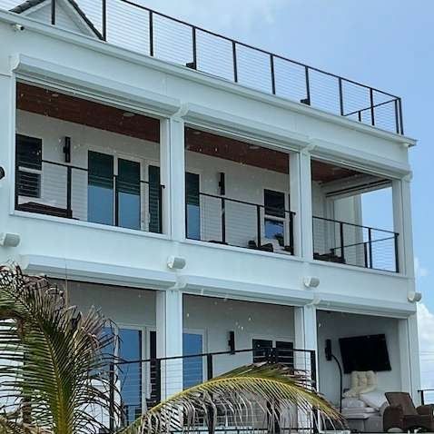 A multi-story white house with large balconies, black railings, and glass doors against a clear blue sky.
