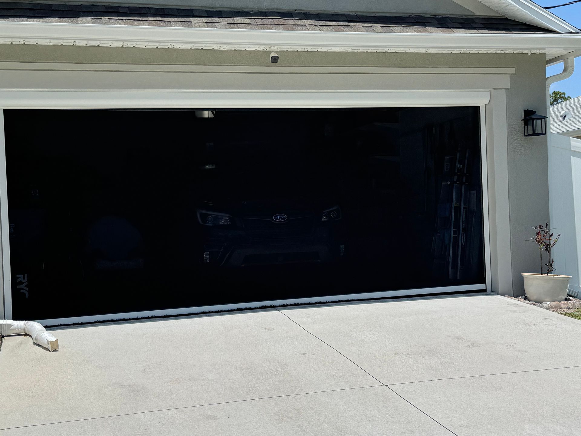 A black mesh screen installed on a suburban garage door opening, shown on a sunny day.