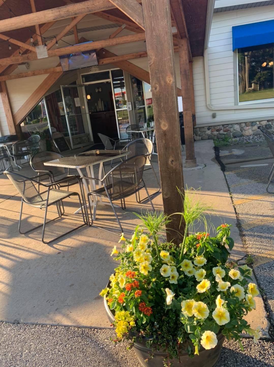 A potted plant with yellow flowers is in front of a restaurant with tables and chairs.