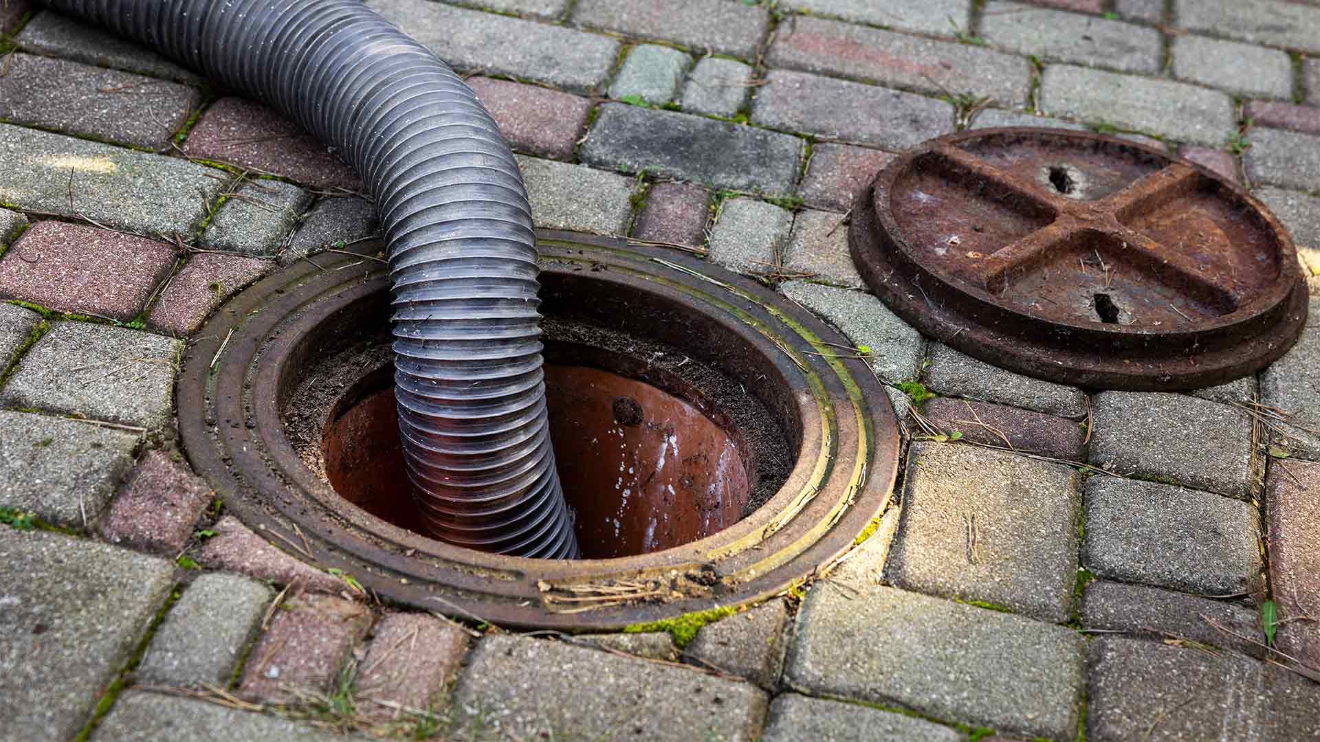 A hose is coming out of a manhole cover on a brick sidewalk.