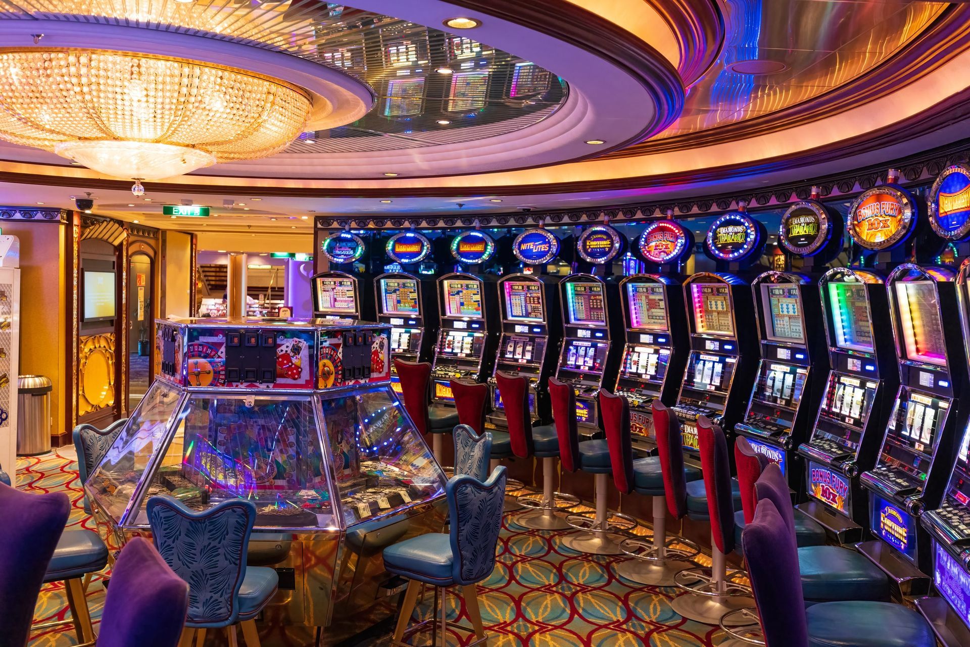 Colorful casino gaming room with rows of slot machines and patterned carpet under warm ceiling lights