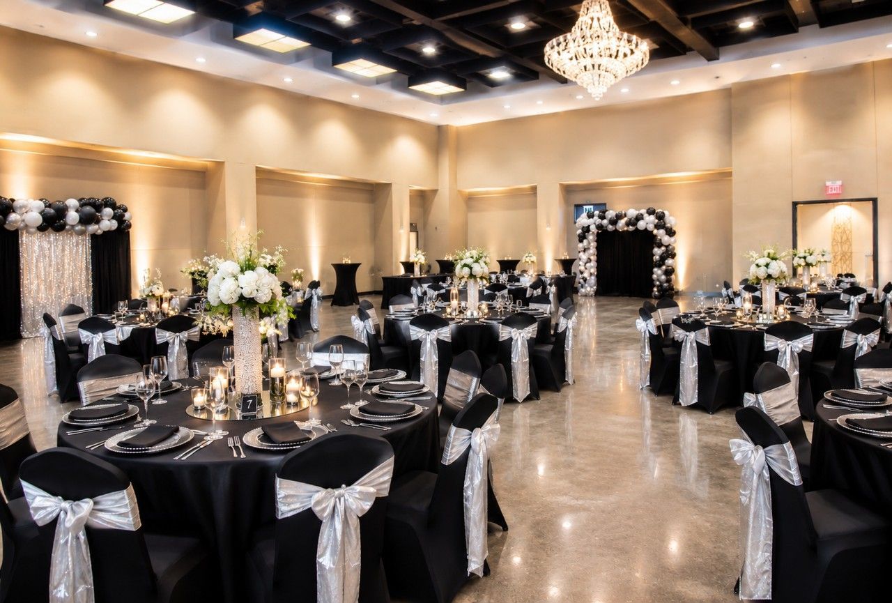 Elegant banquet hall set for a formal event, with black tablecloths, white chair sashes, and chandeliers.