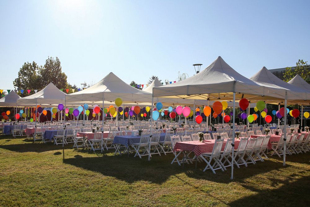 Outdoor party setup with white tents, colorful balloons, and rows of tables and chairs on a grassy field