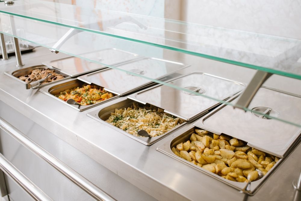 Empty cafeteria-style buffet line with metal food trays under a glass sneeze guard